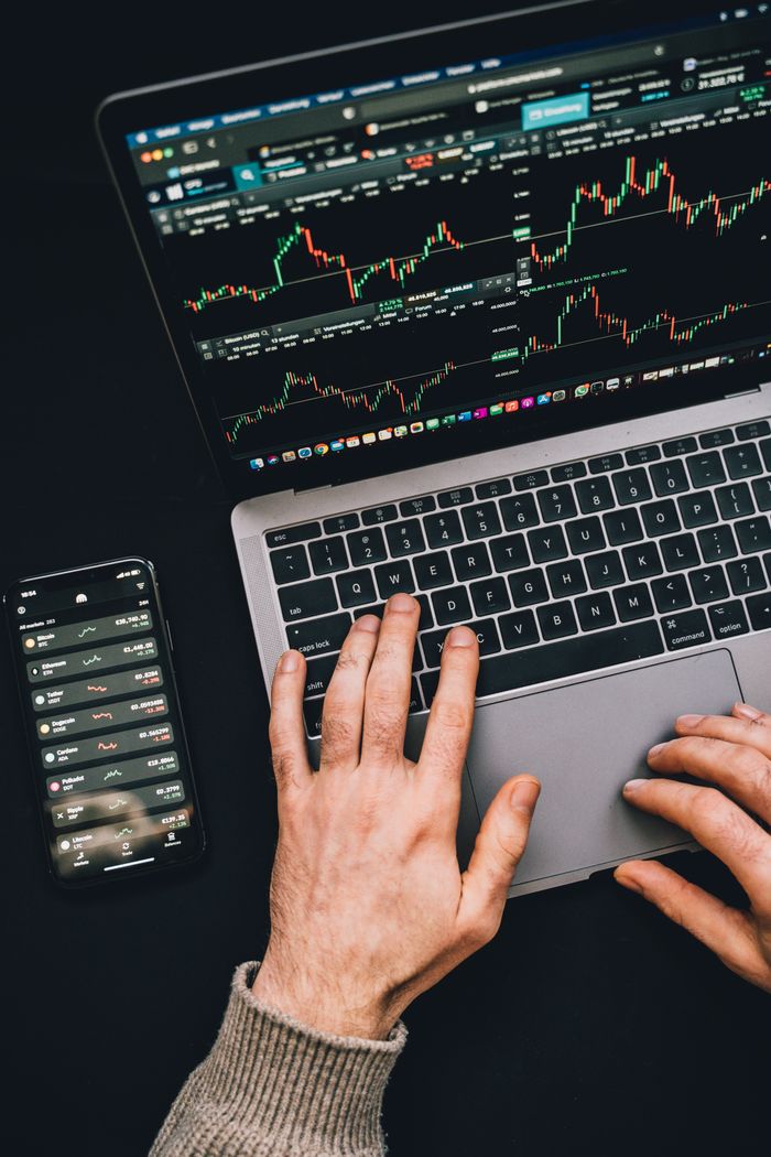 mission-img Hands typing on a laptop with cryptocurrency charts and smartphone display in view, focusing on digital finance.